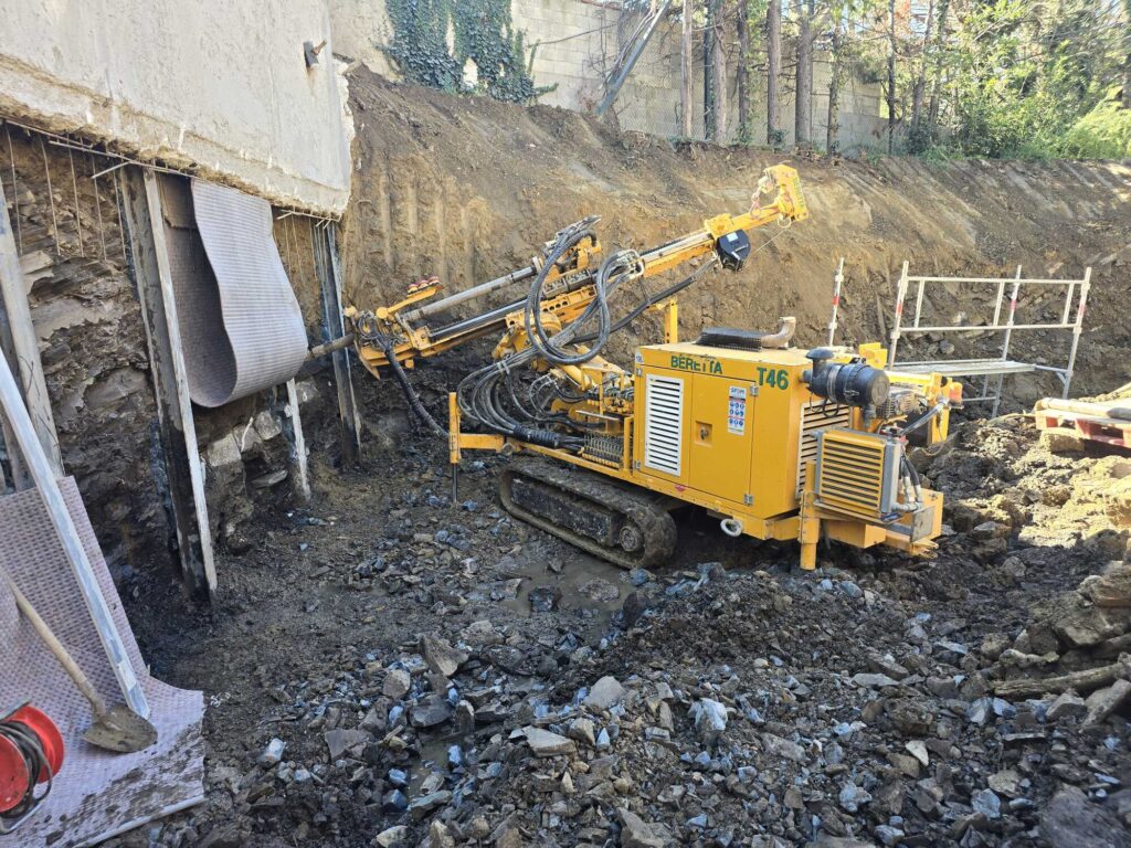 Foreuse Beretta T46 jaune stabilisant un talus boueux sur un chantier de fondations et mur de soutènement.
