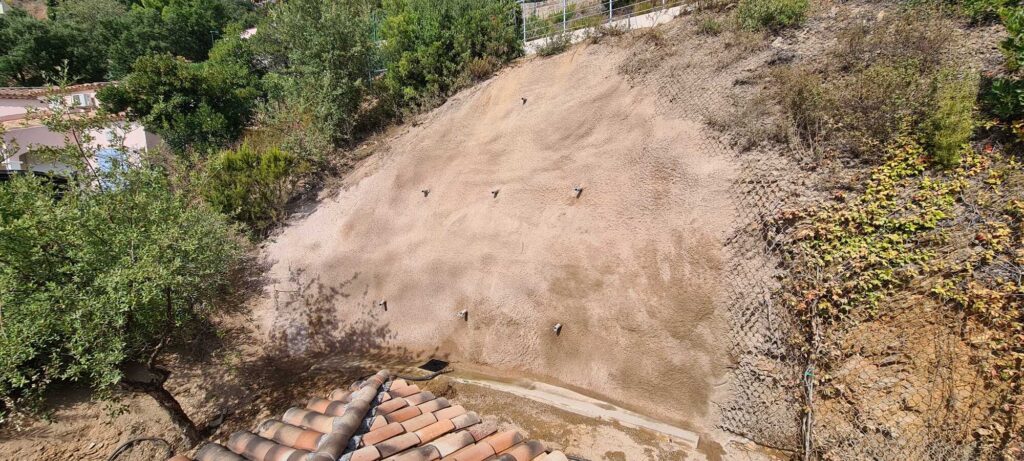 Mur de soutènement en béton projeté avec clous d'ancrage pour sécuriser un talus au-dessus d'une maison.